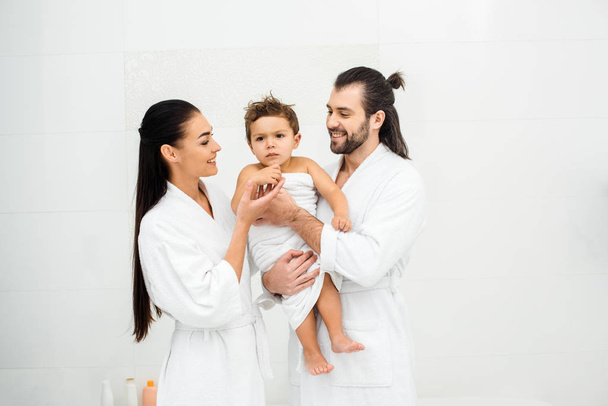 Rodzice, patrząc na syna w biały ręcznik i uśmiechając się  - Zdjęcie, obraz