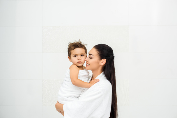 Mom looking at son in towel and smiling on white - Photo, Image