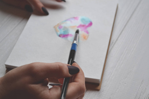 Χρώματα γυναίκα σε ένα sketchbook. Εργαλεία για τη ζωγραφική στο λευκό ξύλινο γραφείο. Έργο της ζωγράφου. - Φωτογραφία, εικόνα