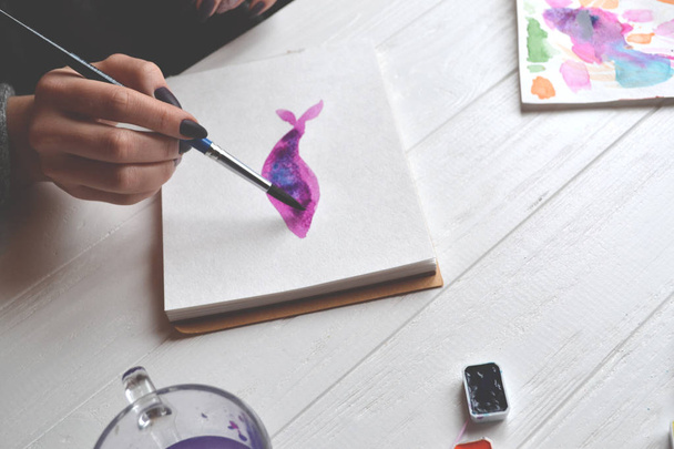 Χρώματα γυναίκα σε ένα sketchbook. Εργαλεία για τη ζωγραφική στο λευκό ξύλινο γραφείο. Έργο της ζωγράφου. - Φωτογραφία, εικόνα