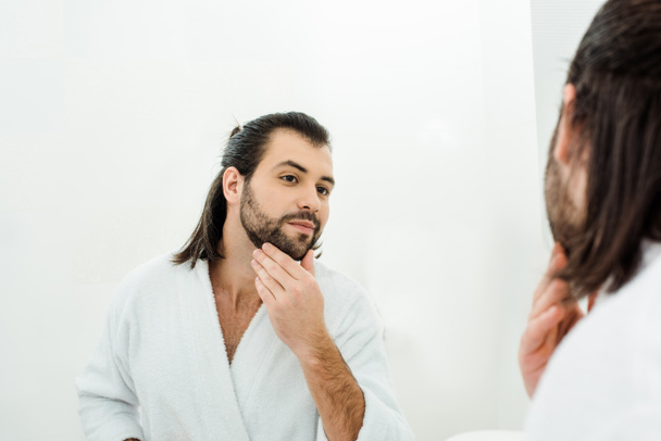 Hombre guapo tocando la barba y mirando en el espejo
  - Foto, imagen