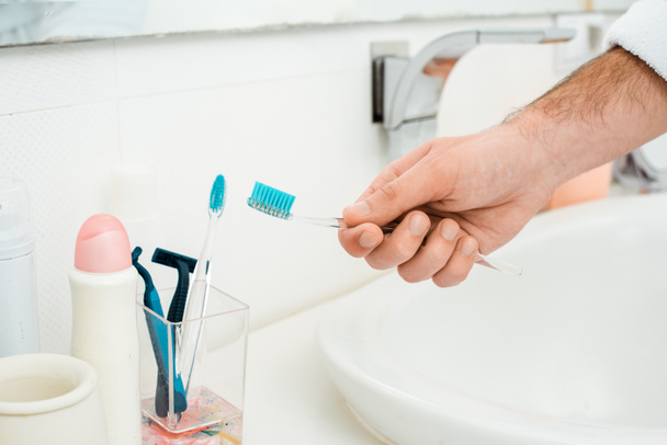 vista recortada de las manos masculinas añadiendo pasta de dientes en el cepillo de dientes
 - Foto, Imagen