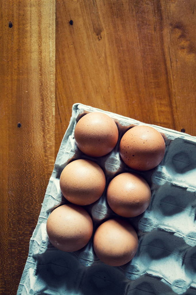Seis ovos crus marrons da galinha na bandeja cinzenta que encontra-se na tabela de madeira, espaço da cópia
 - Foto, Imagem