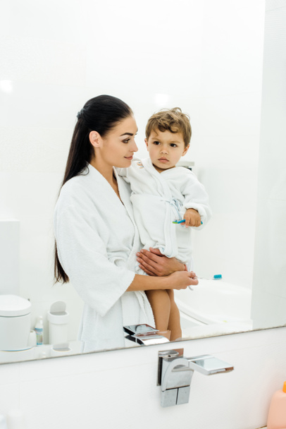 mother and son in white bathrobes brushing teeth together in bathroom - Foto, Imagen