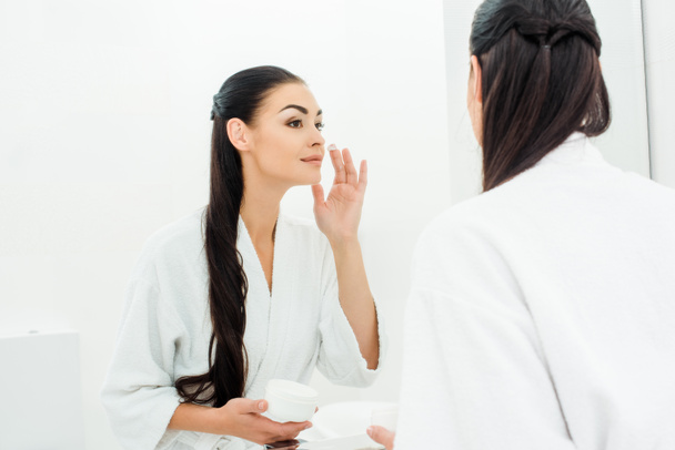 mujer con piel perfecta aplicando crema facial en el baño
 - Foto, Imagen