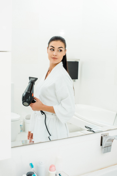 beautiful woman styling long hair with hairdryer in bathroom - Photo, Image