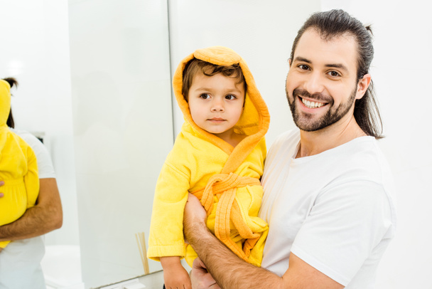 onnellinen hymyilevä isä tilalla poika keltainen kylpytakki
 - Valokuva, kuva