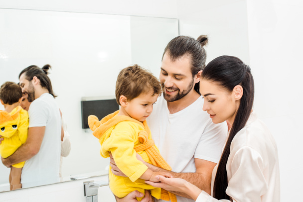 tender young parents holding cute son in yellow bathrobe - Foto, immagini
