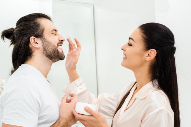 smiling woman applying face cream on man nose in bathroom - Foto, immagini