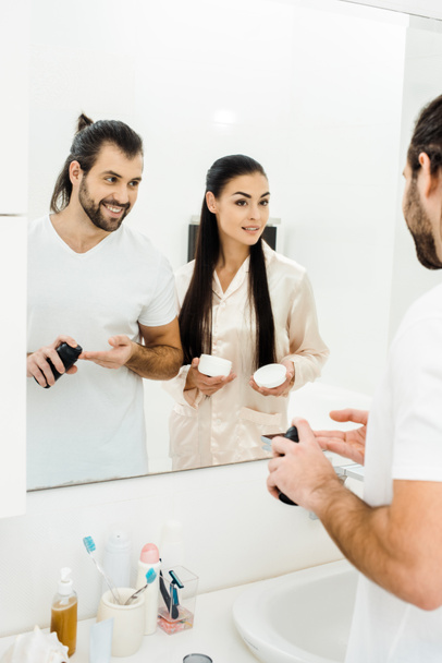 attractive wife holding body cream while handsome husband applying shaving foam - Photo, image