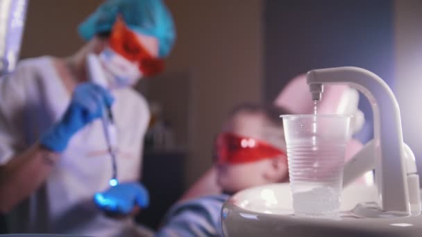 Tandheelkunde, geneeskunde. Tandarts werken met de lamp. Water gieten in de plastic beker. - Video