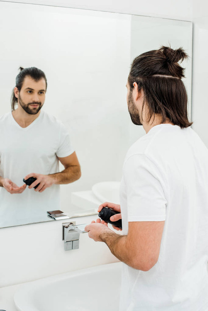 Hombre sosteniendo espuma de afeitar y mirando en el espejo
 - Foto, Imagen