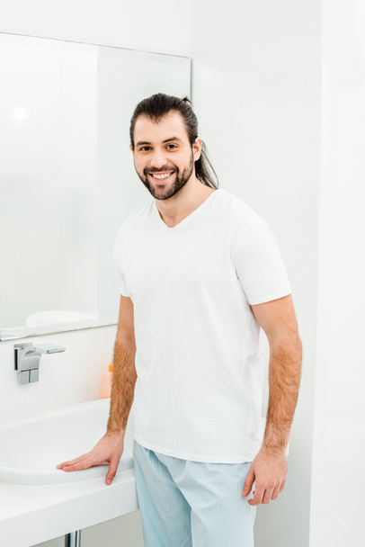 Jonge man in het witte T-shirt glimlachend in badkamer - Foto, afbeelding