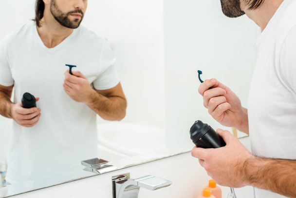 Homem segurando nas mãos acessórios de barbear na frente do espelho no banheiro
 - Foto, Imagem
