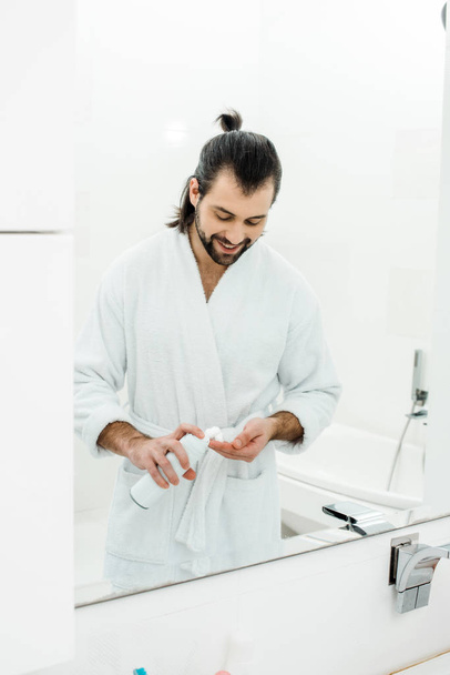 Handsome man holding shaving foam and smiling in front of mirror - Fotoğraf, Görsel