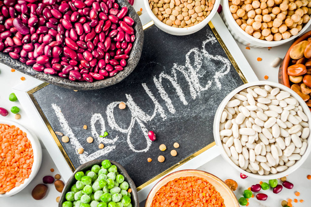 Various assortment of legumes - beans, soy beans, chickpeas, lentils, green peas. Healthy eating concept. Vegetable proteins. White marble background copy space top view - Photo, Image