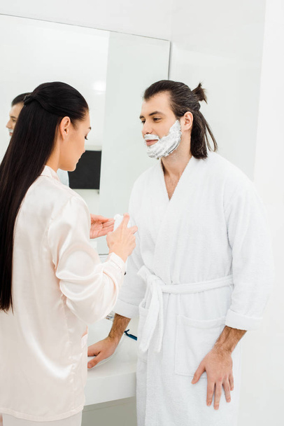 Mujer aplicando espuma de afeitar en la cara del marido
  - Foto, imagen