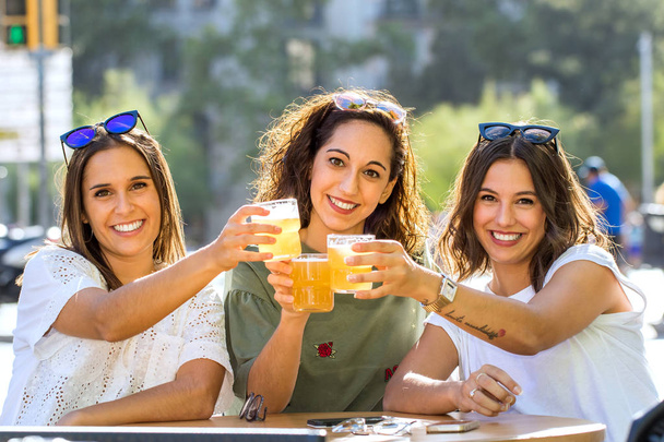 Ritratto ravvicinato di tre fidanzate che bevono insieme sulla terrazza urbana. Giovani donne che guardano la fotocamera fare un brindisi
. - Foto, immagini