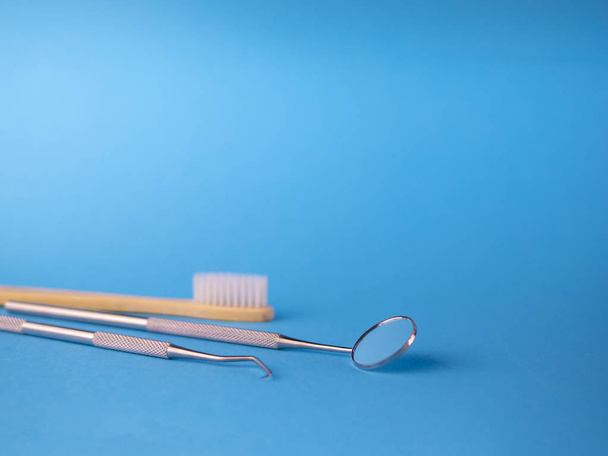 Dentist tools in dental office: dentist mirror and hook, white wooden toothbrush. Dental Hygiene and Health conceptual image. Blue background with copy space for text - Photo, image