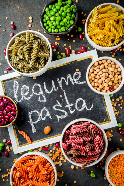 Trend healthy food, vegan diet concept. Multi colored legume pasta with raw beans. Beans, chickpeas, green peas, lentils. Copy space top view - Photo, Image