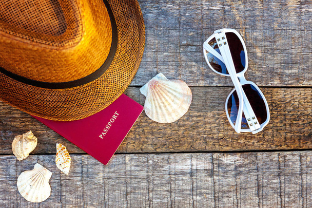 Flat Lay with hat, passport, sunglasses and shell on rustic trendy old vintage wooden background. Vacation travel summer weekend sea adventure trip concept - Photo, Image