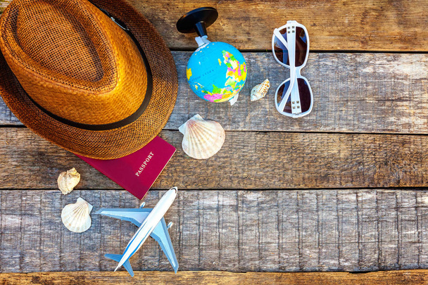 Flat Lay with hat, plane, passport, globe, sunglasses and shell on rustic trendy old vintage wooden background. Vacation travel summer weekend sea adventure trip concept - Photo, Image
