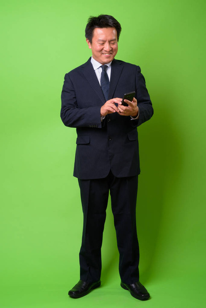 Mature Japanese businessman against green background - Фото, изображение