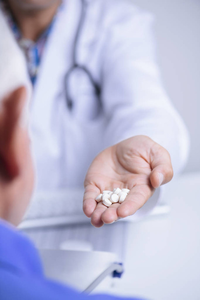 gros plan d'un médecin caucasien, vêtu d'un manteau blanc, donnant quelques pilules à un patient caucasien âgé, assis à la fois à un bureau de médecins
 - Photo, image