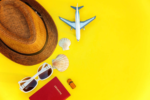 Flat Lay with hat, plane, passport, sunglasses and shell on yellow colourful trendy modern fashion background. Vacation travel summer weekend sea adventure trip concept - Photo, Image