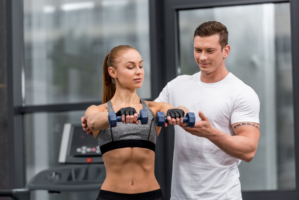 handsome personal trainer helping sportswoman exercising with dumbbells in gym - Φωτογραφία, εικόνα