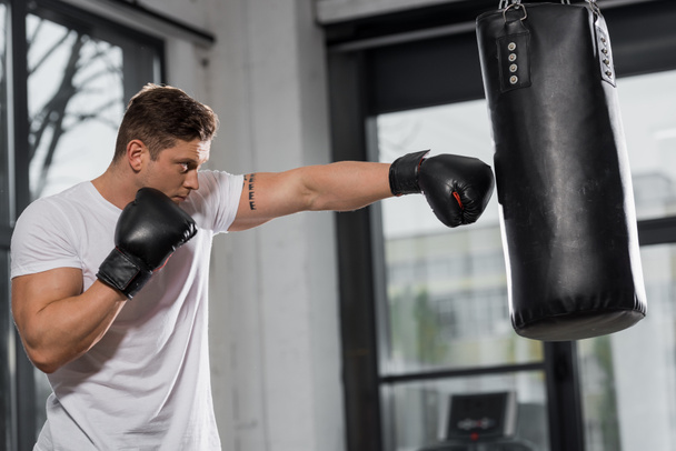 side view of handsome muscular boxer exercising with punching bag in gym - Φωτογραφία, εικόνα