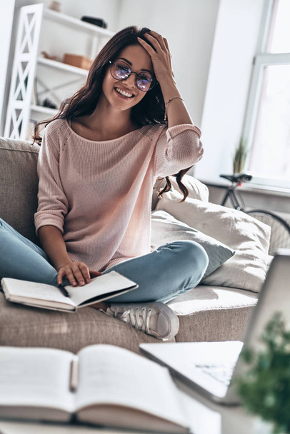smiling happy Beautiful young woman in glasses studying while sitting on sofa at home with book - Photo, Image