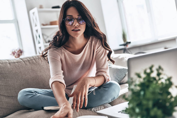 brunette young woman in glasses studying while sitting on sofa at home - Photo, Image