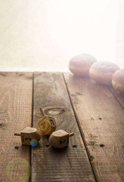 Still life for jewish holiday Hanukkah with 3 donuts and 3 dreidels on wooden rustic table.Hanukkah celebration concept.Lens Fleur copy space. Focus on the Deidls.copy space - Photo, Image