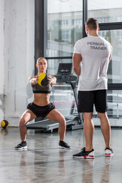 back view of personal trainer watching at sportswoman training with fitness ball in gym - Fotoğraf, Görsel