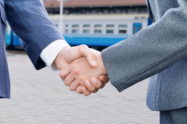 Two businessman are shaking their hands at the overhead railway background. The concept is the interaction of different business fields. - Photo, Image