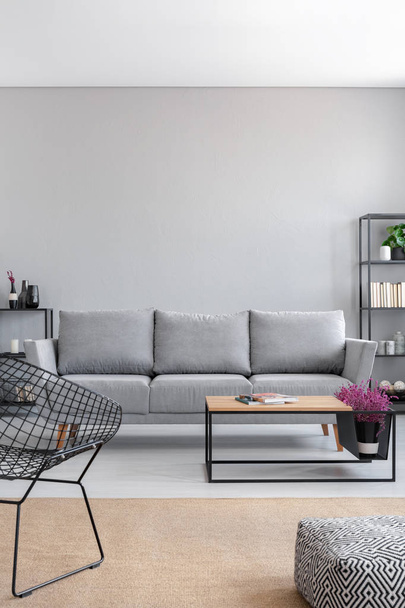 Real photo of a simple living room interior with a grey sofa, armchair, coffee table and brown rug. Empty wall, place your graphic - Photo, Image