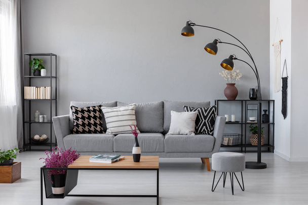 Copy space on the real photo of industrial living room with dark metal furniture and grey couch with patterned pillows - Photo, image