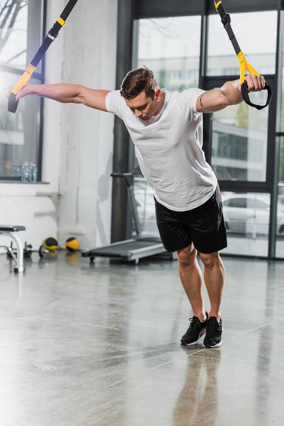 handsome muscular bodybuilder working out with suspension straps in gym - Fotografie, Obrázek