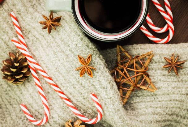 Karácsonyi gőzölgő csésze forró glint bor, fűszerek, ánizs, cookie-k, csillag alakú, piros cukorka, bors, fenyő kúpok és szürke sál, fából készült háttér. Nézd meg felülről. Lapos feküdt. - Fotó, kép