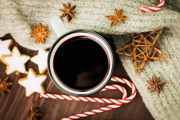 Christmas hot steaming cup of glint wine with spices, anise, cookies in a shape of star, red candies, pepper and gray scarf on wooden background. View from above. Flat lay. - Photo, Image