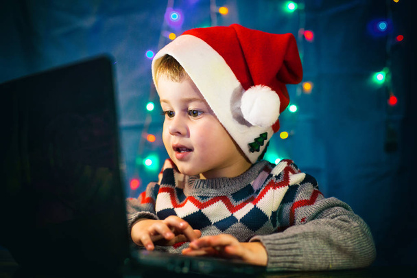 小さな子供は、ラップトップ コンピューターでサンタ クロースに手紙を書きます。冬の休日のクリスマスと新年のコンセプト. - 写真・画像