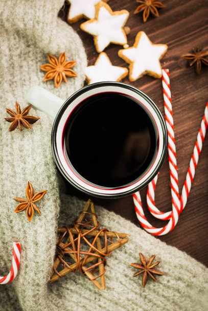 Christmas hot steaming cup of glint wine with spices, anise, cookies in a shape of star, red candies, pepper and gray scarf on wooden background. View from above. Flat lay. - Photo, Image