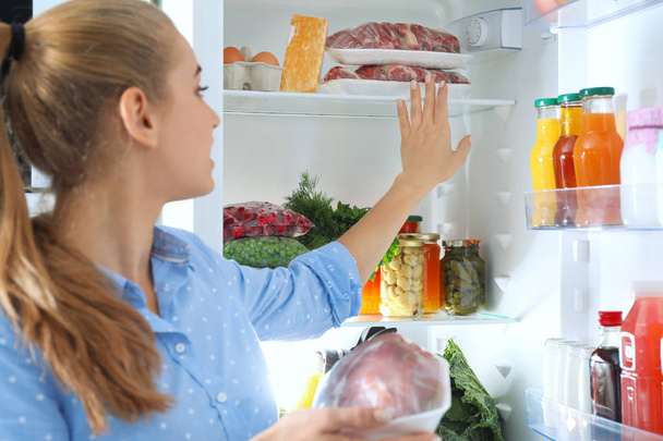 Woman taking fresh meat out of refrigerator in kitchen - Photo, Image