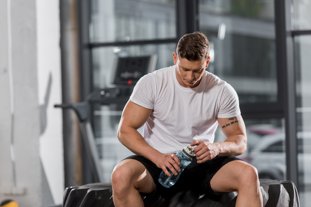 beau bodybuilder athlétique assis sur le pneu avec bouteille d'eau sportive dans la salle de gym
 - Photo, image