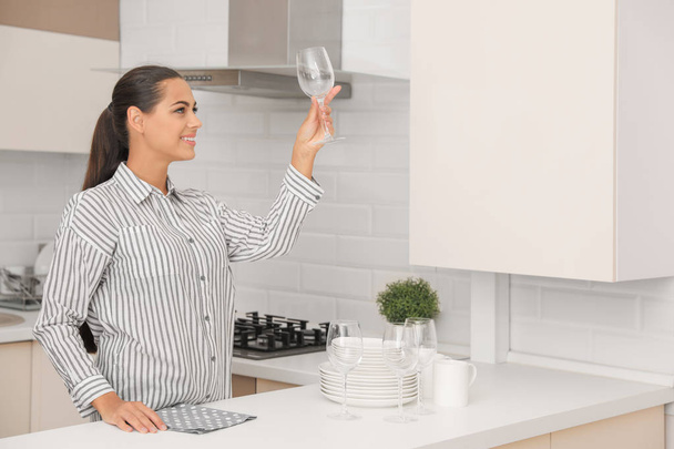 Young woman holding clean glass in kitchen. Dish washing - Foto, immagini