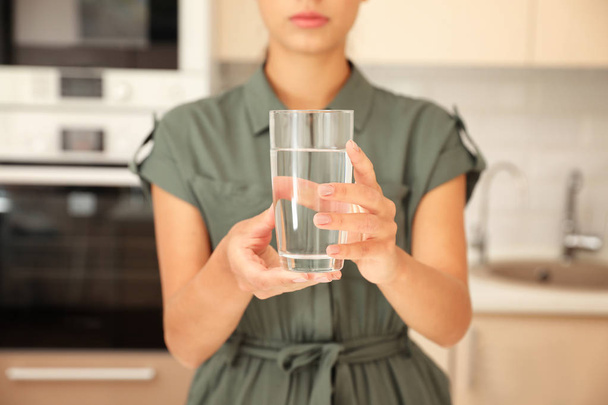 Woman holding glass with pure water in kitchen, closeup - Φωτογραφία, εικόνα