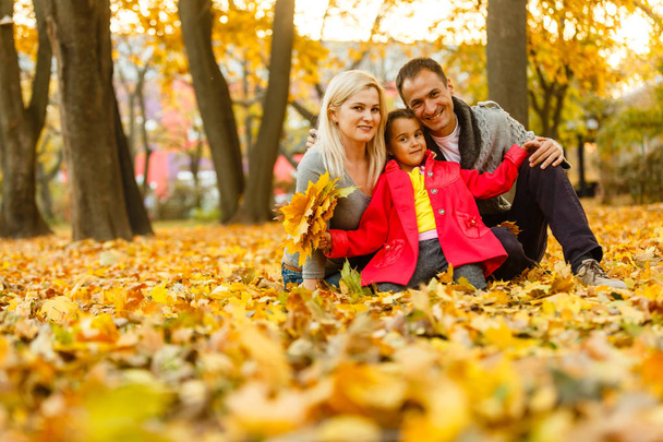 ευτυχισμένη οικογένεια ξοδεύουν χρόνο μαζί ενώ ξεκουραζόταν σε πορτοκαλί φθινοπωρινά φύλλα εξωτερική  - Φωτογραφία, εικόνα