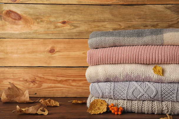 Stack of warm clothes with autumn leaves on wooden table. Space for text - Fotografie, Obrázek