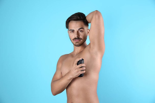 Young man using deodorant on color background - Φωτογραφία, εικόνα